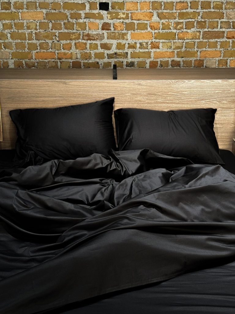 A bed with black bed sheets and pillows.
