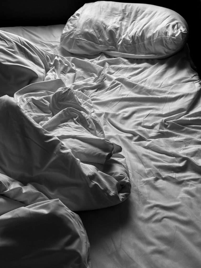 An un-made bed with bed sheets and pillows.
