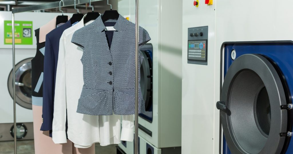 Garments that have been dry cleaned next to a dry cleaning machine.